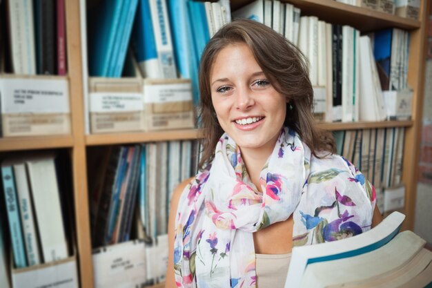 Glimlachende vrouwelijke student tegen boekenrek in de bibliotheek