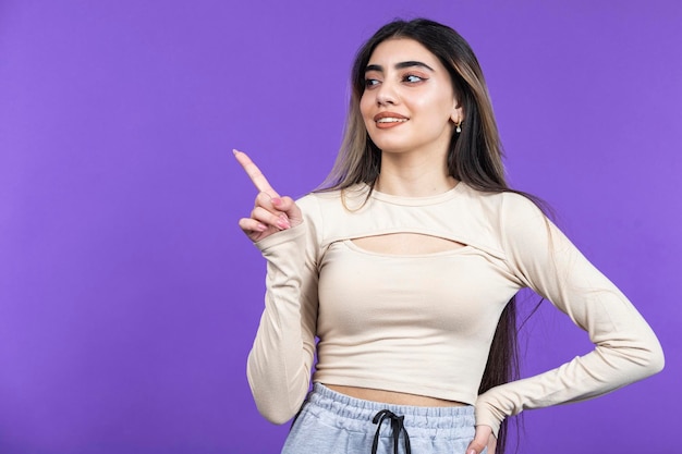 Glimlachende vrouwelijke wijsvinger opzij en staat op paarse achtergrond Foto van hoge kwaliteit