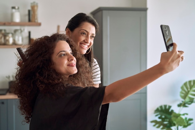 Glimlachende vrouwen die een selfie maken terwijl ze hun haar knippen