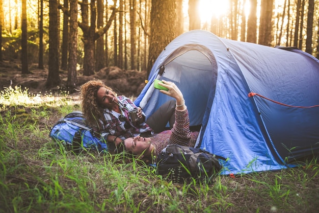 Glimlachende vrouwen nemen een selfie bij een tent in het bos.