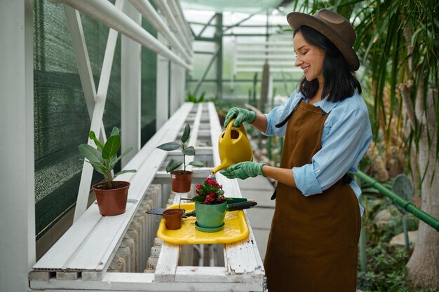 Glimlachende vrouwentuinman die bij botanisch landbouwbedrijf werken. broeikas werknemer planten bloem in pot drenken zaailingen