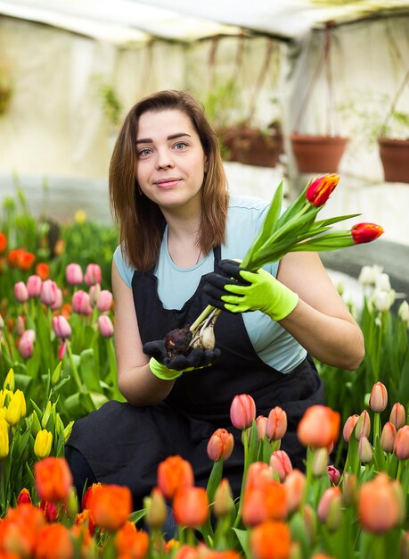 Glimlachende vrouwentuinmanbloemist die een boeket bloemen houdt die zich in een serre bevinden waar de tulpen cultiveren