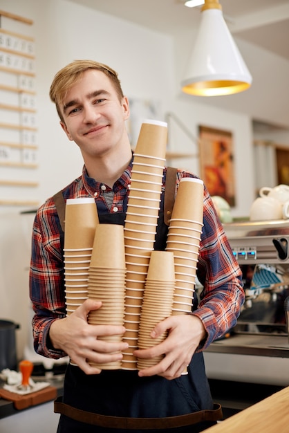 Glimlachende werknemer barista in schort met veel wegwerp papieren bekertjes drinken in café