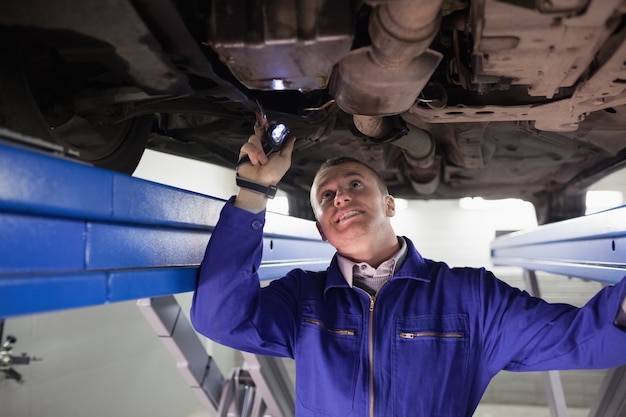 Glimlachende werktuigkundige die een auto met een flitslicht verlicht