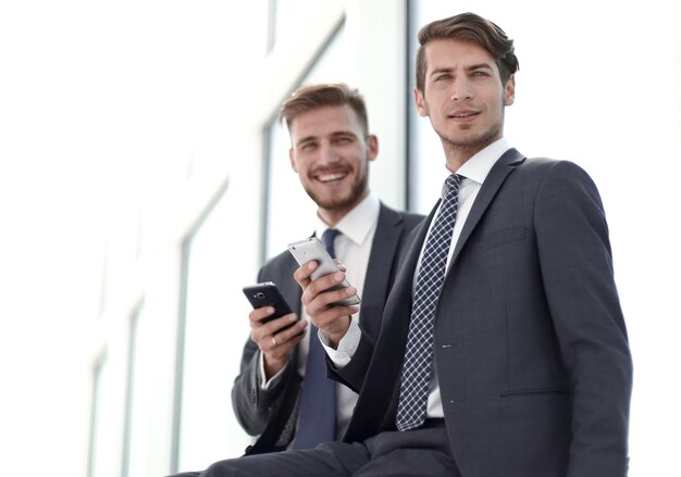 Glimlachende zakencollega's met smartphones die in de kantoorlobby zittenfoto met kopieerruimte