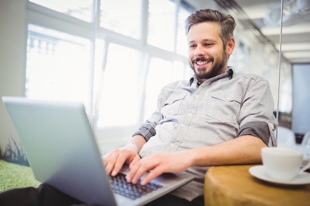 Glimlachende zakenman die aan laptop in bureau werkt