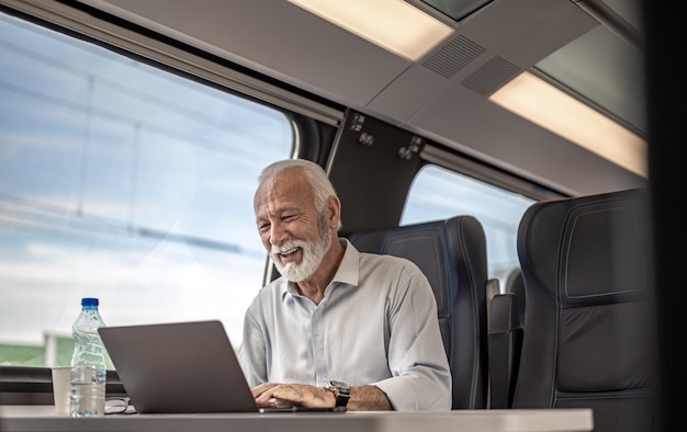 Glimlachende zakenman die aan laptop werkt terwijl hij op de passagierstrein reist