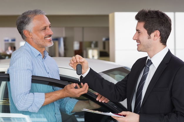 Glimlachende zakenman die autosleutel geeft aan gelukkige klant