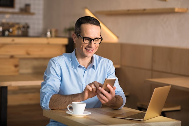 Glimlachende zakenman die een bril draagt met smartphone in café