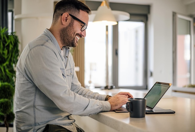 Glimlachende zakenman die op laptop werkt terwijl hij aan een bureau zit op kantoor