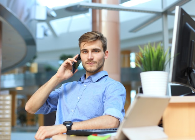 Glimlachende zakenman die staat en mobiele telefoon gebruikt op kantoor