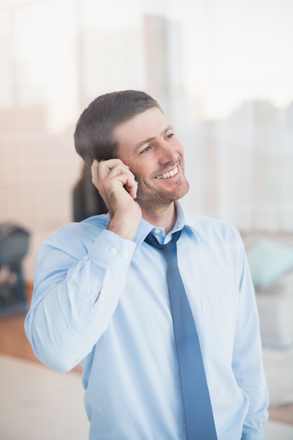 Glimlachende zakenman die uit venster op de telefoon kijkt