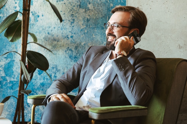 Glimlachende zakenman draagt pak praten op mobiele telefoon zittend in het café