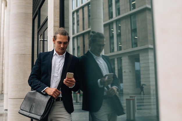 Glimlachende zakenman met een smartphone terwijl hij bij het gebouw staat