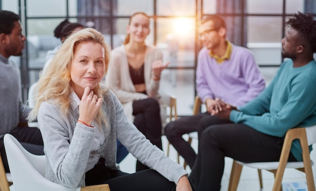 Glimlachende zakenvrouw die naar de camera kijkt tijdens een seminar met haar collega's in de buurt