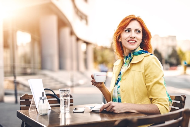 Glimlachende zakenvrouw drinkt koffie in een straatcafé.