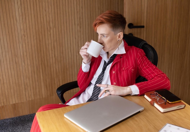 Glimlachende zakenvrouw in rood pak met een koffiekopje die op kantoor zit