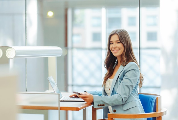 glimlachende zakenvrouw manager ontwerper met een laptop die online werkt en naar de camera kijkt in het kantoor