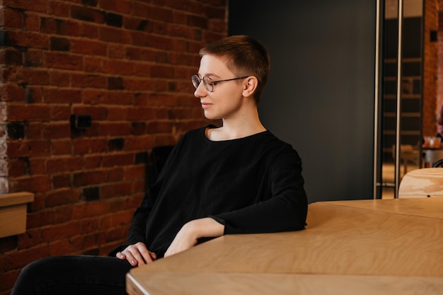 Foto glimlachende zakenvrouw met kort haar in een bril en een zwarte trui die aan tafel zit