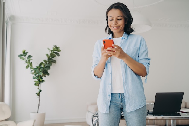 Glimlachende zakenvrouw met smartphone typen bericht in zakelijke app leest werkend nieuws op kantoor