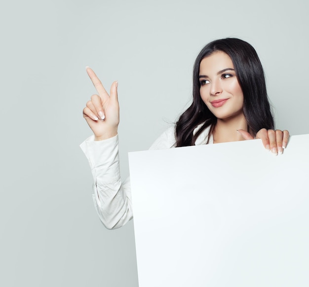 Glimlachende zakenvrouw met witte blanco papier banner achtergrond en wijzende zelfverzekerde student vrouw business en onderwijs concept