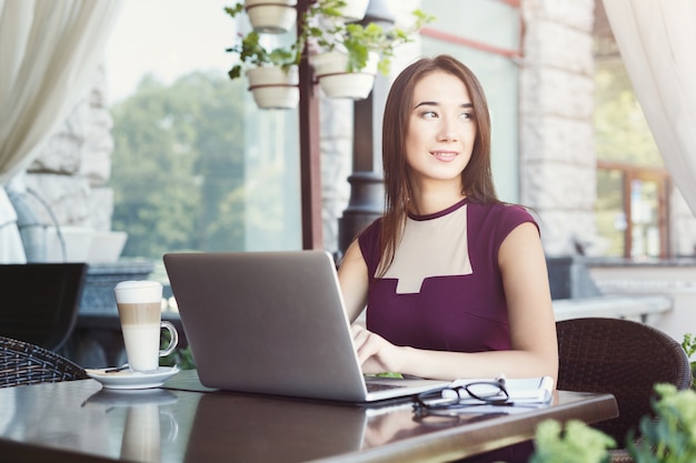 Glimlachende zakenvrouw werken met laptop zittend op zomerterras café. Lifestyle portret van jonge zakenvrouw. Technologie en online communicatieconcept