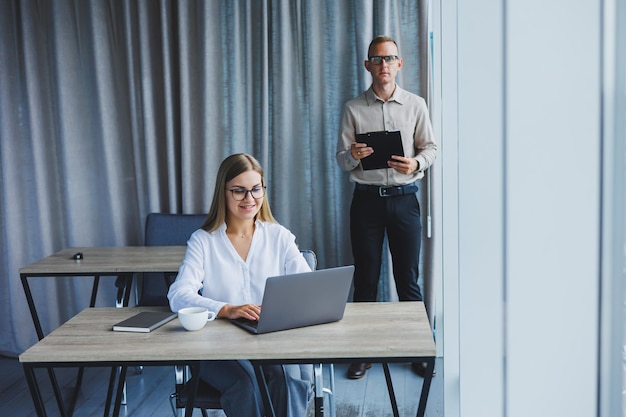 Glimlachende zakenvrouw zittend aan een tafel met een laptop die haar rug naar haar partner achter het bureaublad houdt Het concept van succesvol teamwerk