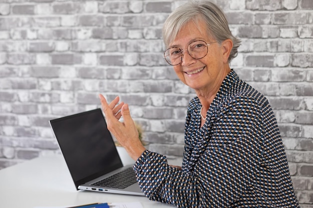 Glimlachende zelfverzekerde oudere zakenvrouw die met een collega praat terwijl ze op een laptop werkt