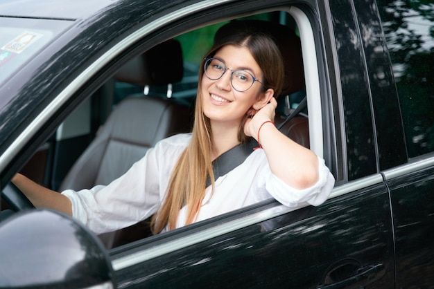 Glimlachende zelfverzekerde vrouw die nieuwe auto rijdt en naar de camera kijkt. vervoersconcept: