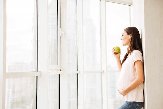 Glimlachende zwangere jonge vrouw die groene appel eet