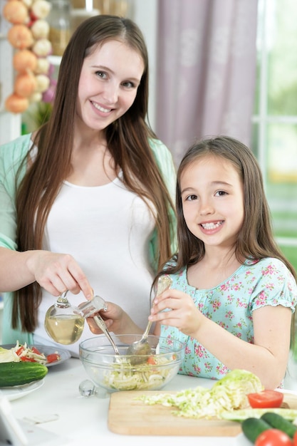 Glimlachende zwangere moeder en dochter die samen koken bij keuken