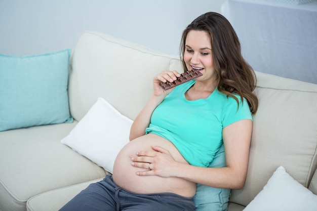 Glimlachende zwangere vrouw die chocolade op laag eet