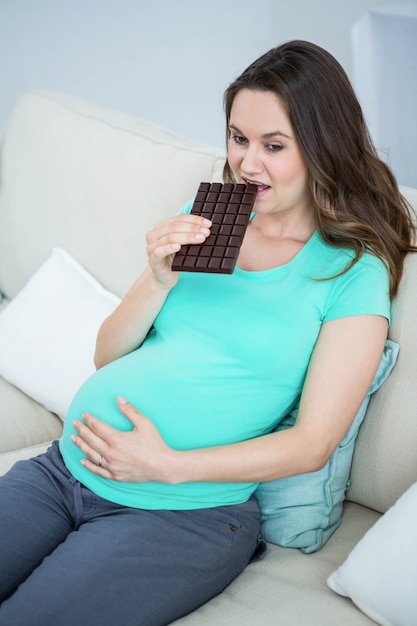 Glimlachende zwangere vrouw die chocolade op laag eet