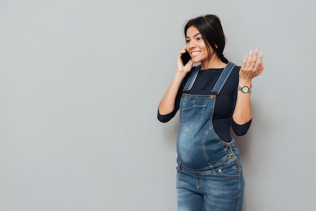 Glimlachende zwangere vrouw die door mobiele telefoon spreekt