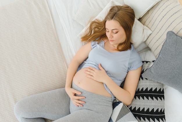 Glimlachende zwangere vrouw die thuis in haar bed in de slaapkamer rust