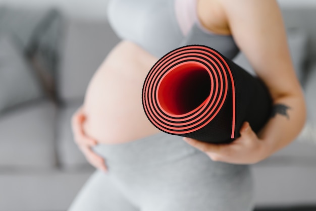 Glimlachende zwangere vrouw in sportkleding klaar voor ochtendgymnastiek of oefening. Gelukkige jonge vrouw volgt een gezonde levensstijl tijdens de zwangerschap, houdt een yogamat vast voor Pilates of stretching.