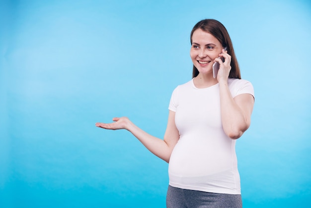 Glimlachende zwangere vrouw met smartphone op het gehoor in gesprek met haar vriend of echtgenoot terwijl ze iets geïsoleerd uitlegt of bespreekt