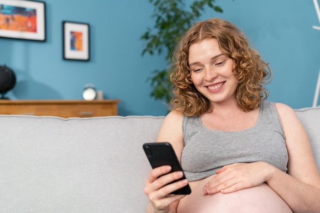 Glimlachende zwangere vrouw met smartphone thuis mooie zwangere vrouw die mobiele telefoon gebruikt