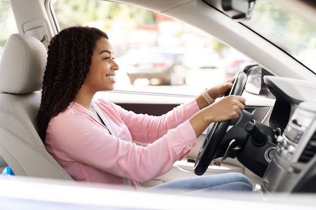 Glimlachende zwarte vrouw die nieuwe auto rijdt in de stad
