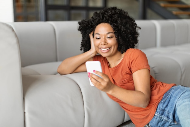 Glimlachende zwarte vrouw die thuis video's op haar smartphone kijkt