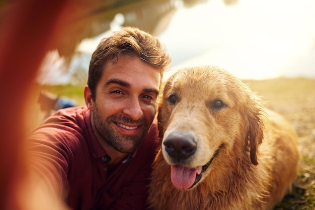 Glimlachjongen Bijgesneden opname van een knappe jonge man en zijn hond die selfies nemen bij een meer in het park