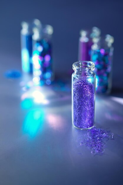 Glitter products in transparent bottles closeup Various glitter powrer and particles in neon blue purple and turquoise shades on dark background