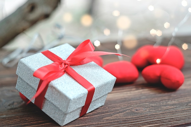 Glitter silver gift box placed on wooden floor with heart on the background.