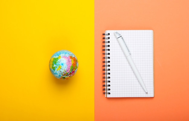 Globe and notebook on yellow orange background. Top view. Minimalism. Education concept, geography