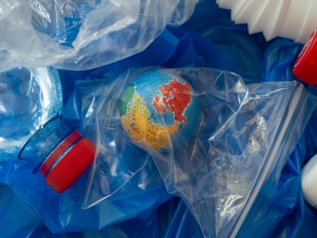 プラスチック廃棄物の山の中のビニール袋に入った地球儀