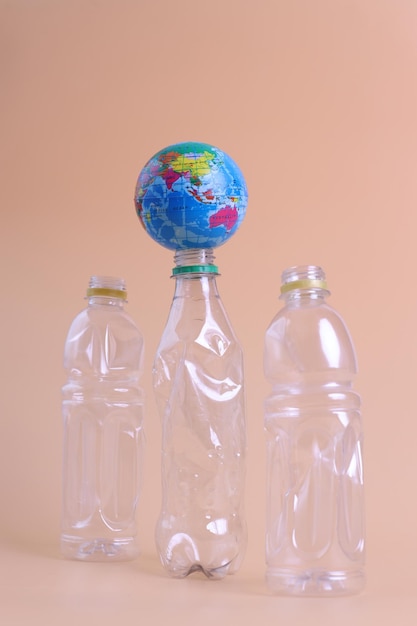 A globe on the top of single use transparent plastic bottles on\
a pastel background. the problem of