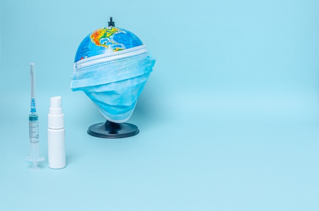 Photo globe with a protective medical mask, syringe, white capacity for antiseptics on a blue background