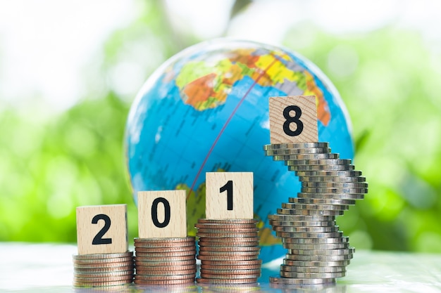 Photo globe behind a wooden numbers 2018 on growing stack of coins using as achievement concept.