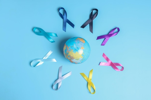 Globes surrounded by colorful awareness ribbons on blue background. world cancer day.