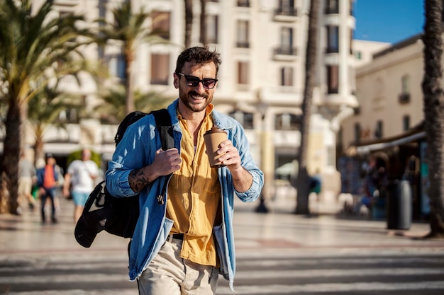 A globetrotter with backpack and coffee is visiting Spain while walking on the street